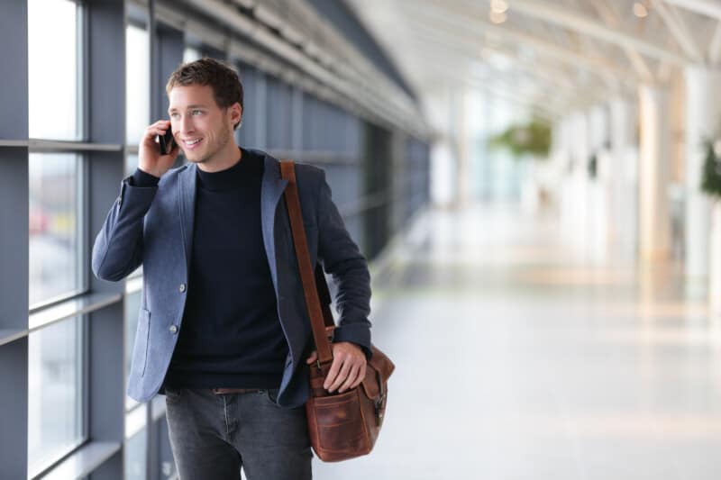 Article: sling bag vs messenger bag Image: Urban business man talking on smart phone, with messenger bag