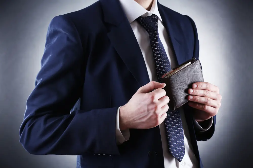 man putting leather wallet into suit pocket